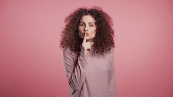 Positive Girl Holding Finger on Her Lips Over Pink Background. Gesture of Shhh alt