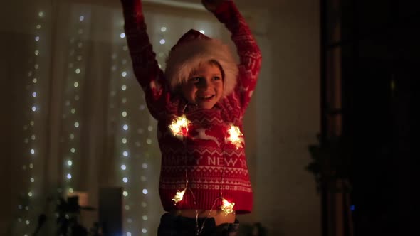 Excited Christmas Boy Jumping Dancing in Santa Hat at Home Evening alt