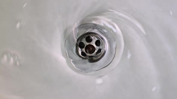 Water swirling down the drain hole of a stainless steel sink, close up