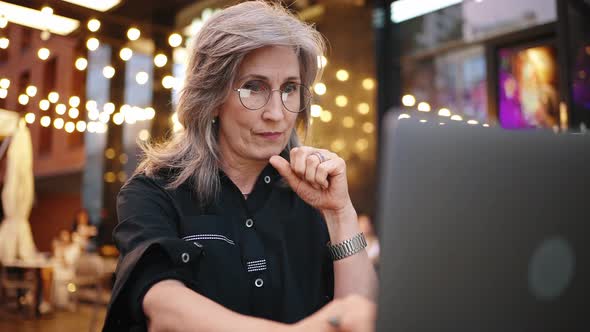 Portrait of Beautiful Senior Businesswoman Sitting at Cafe with Laptop Looking Carefully on the alt