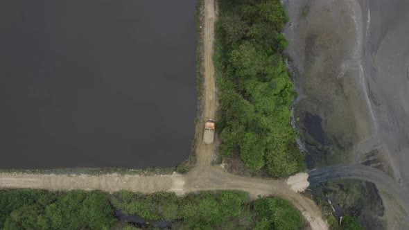 A large truck filled with sand riding over a small dirt road  alt