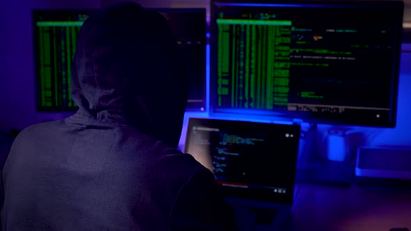 Man in a Hood Working As a Hacker at the Computer in the Dark Room at Night Hacking the System and