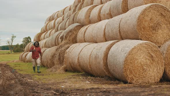 Young African Man, with Pitchfork Over His Shoulder Walking in Front of the Hay Rolls Stack alt