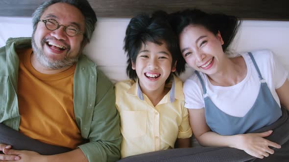 Asian family mom dad and cute son child laying laugh smile on white soft bed