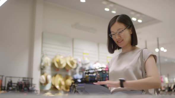Friendly Chinese Woman Paying for Goods with Palm Scan at Fashion Shop alt
