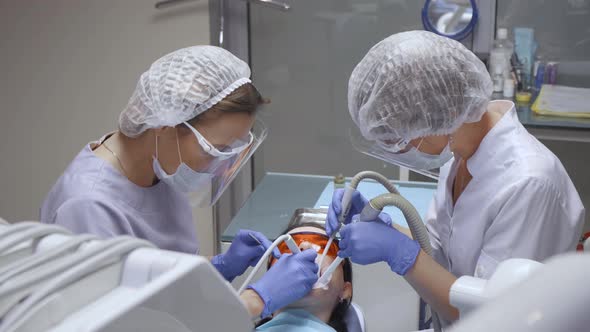 A Professional Dentist And Her Assistant Work With A Female Client Sitting In A Chair alt