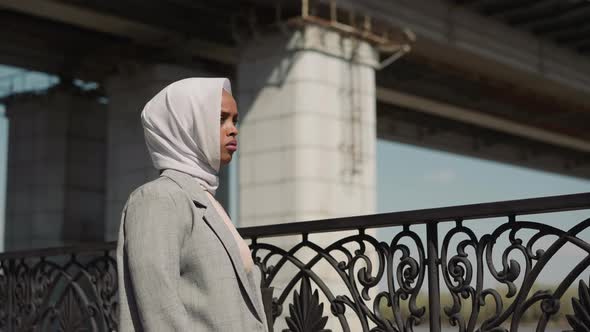 Sad Arabian Woman Stands By Fence on Town Embankment alt