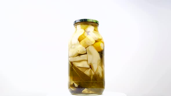 Glass jar of canned zucchini on a white background. 