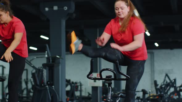 Group Athletic Girls Performing Aerobic Riding Training Exercises on Cycling Stationary Bike in Gym alt