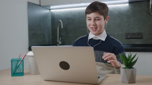 Smiling Boy in Earphones Chatting Online By Video Call with Laptop Computer at Home While Sitting alt