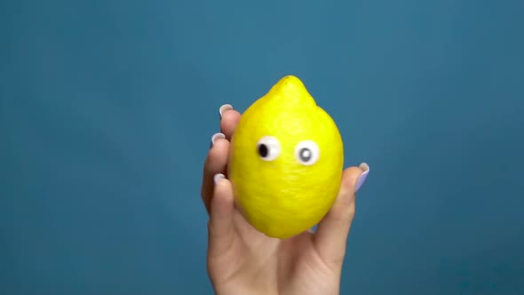 Lemon with Eyes in a Woman Hand Close-up. Lemon Shakes and Twists Eyes ...