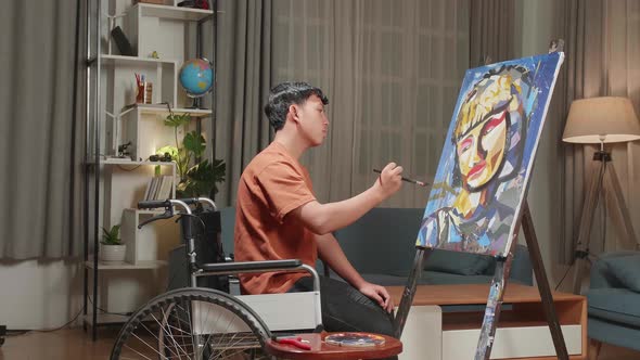 Side View Of An Asian Artist Boy In Wheelchair Painting A Girl On The Canvas alt