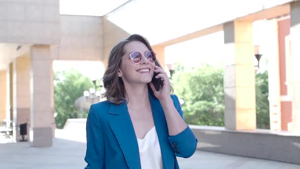 A Woman in a Business Suit Smiles While Talking on the Phone. alt