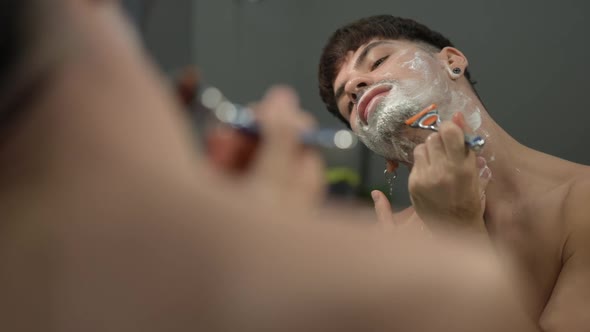 Reflection of Young Man Shaving Chin in Slow Motion at Home in Bathroom alt