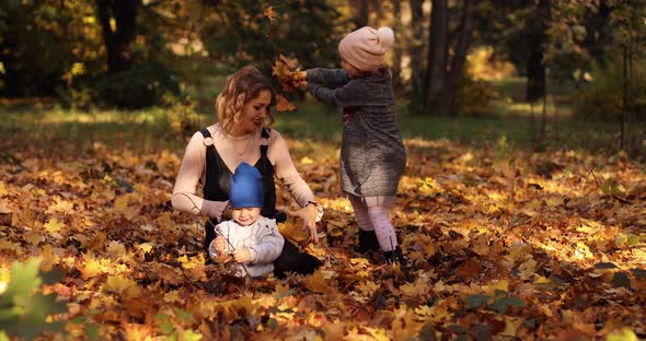 Gorgeous Young Mother with Two Kids Enjoying Sunny Autumn Day on the Foliage