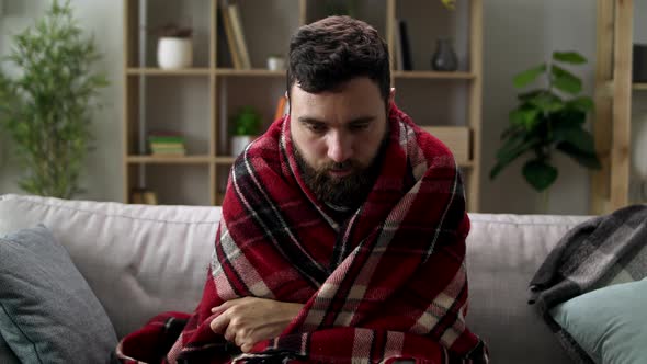 Ill Man with Chills and Wraps Himself in a Blanket on the Sofa in Living Room alt