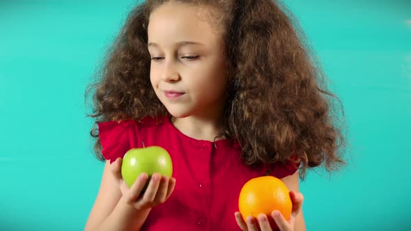Cute Child on Turquoise Background of Holding a Green Apple and Orange and Choice Healthy Eating alt