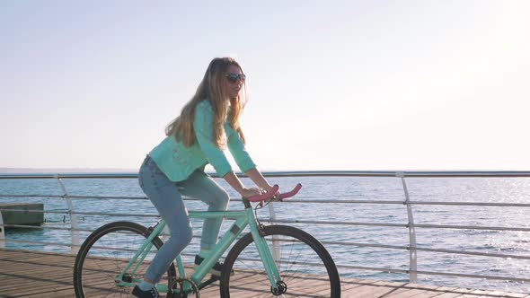 Young Stylish Woman Cyclist Enjoying Fixed Gear Bike Riding Outdoors at Sunrise Near the Sea alt