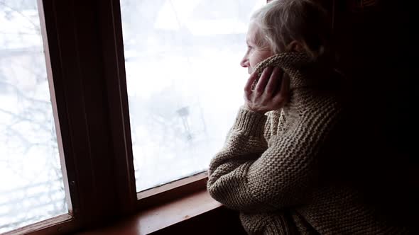 Woman in Old Age Stands at the Window and Looks Alone Into the Distance