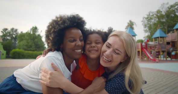 Multiethnic Lesbian Couple and Adopted Little Daughter Hugging on Playground alt