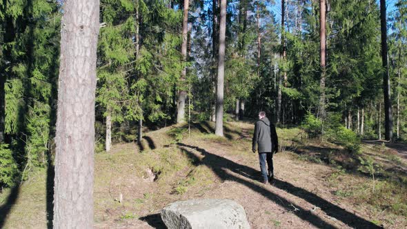 A young guy in dark clothes with short hair walks through the forest