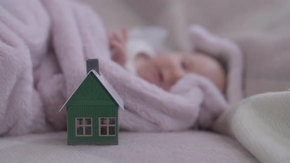 Closeup Toy House on Cozy Bed with Blurred Innocent Baby Girl Sleeping at Background alt