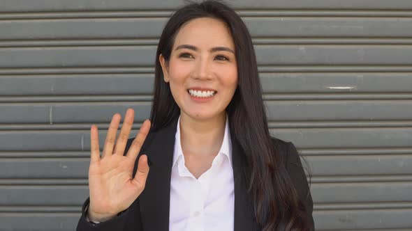Asian smiling businesswoman waving hand to camera