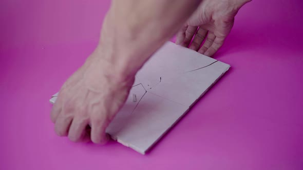 The hands of a man fix the fragments of broken ceramic tiles with a hammer alt