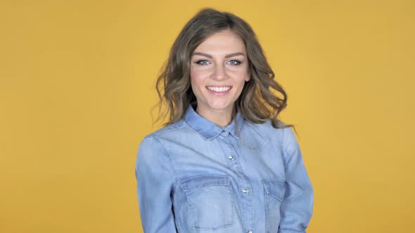 Young Girl Playing with Hairs Turning Around And Smiling Isolated on Yellow Background alt