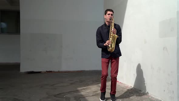 Young Man Is Playing at Saxophone at Street, Rehearsing and Performing Gig Outdoors alt