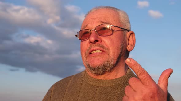 A Grayhaired Man in Sunglasses Speaks Into the Camera Lens Waving His Hand alt