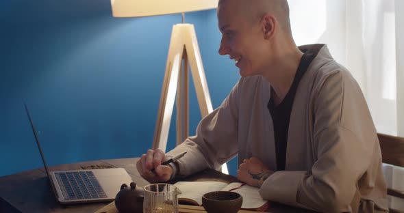 Smiling Woman Freelancer Talking at Video Conference Using Computer and Making Notes Side View alt