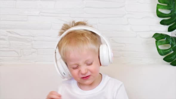 Boy smiles with big white headphones and actively dances with his eyes closed and listens to music