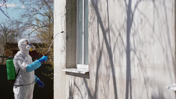 Worker in Protective Suit Sprays a Disinfectant on the Window