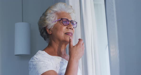 Thoughtful african american senior woman with hand on chin looking out of the window at home alt