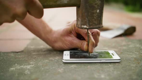 A Man Hammers a Nail Into the Phone on the Concrete Ground in Slow Motion alt