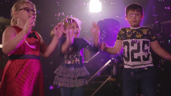Kids Dancing at a Children's Party with Bubble Machine blowing Bubbles in to Air. alt