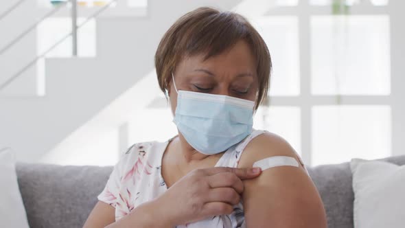 African american senior woman in face mask showing bandage on arm after covid vaccination alt