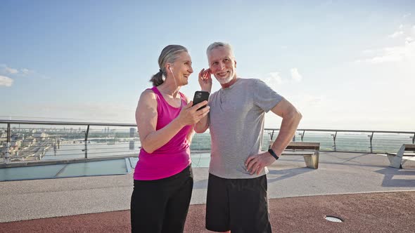 Happy Pensioners Share Headphones Listening Music on Phone alt
