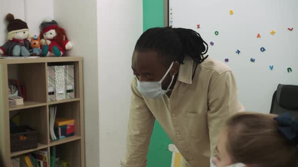 An African American Teacher Teaches a Group of Children at School During a Pandemic alt
