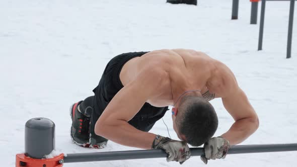 Muscular man training topless on sports field in winter