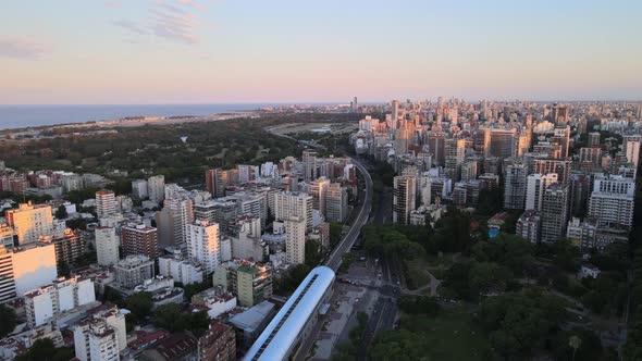 Dolly in flying over a train station surrounded by buildings and parks with Rio de la Plata river in alt