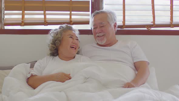 Happiness Two Asian couple elder husband and wife lying on bed together smile and laughing at home alt