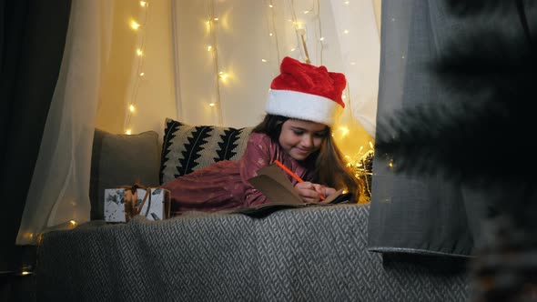 Little Girl Writes a Letter to Santa Claus with Wishes Lying on the Windowsill Decorated with a alt