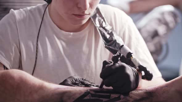 A Session at the Tattoo Salon  Young Man Tattooing Big Letters on the Leg  Looking in the Camera alt