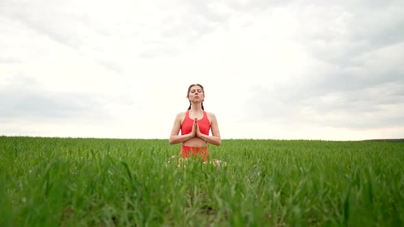 Concentrated Woman in Lotus Pose Doing Meditation with Namaste in Green Field alt
