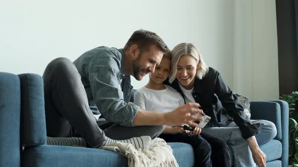 Happy family adult parents with cute school kids children relax on sofa using funny smartphone