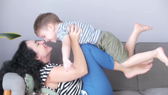 Happy Healthy Family Young Mom Lifting Cute Little Child Son Up Playing Plane on Sofa at Home, Funny alt