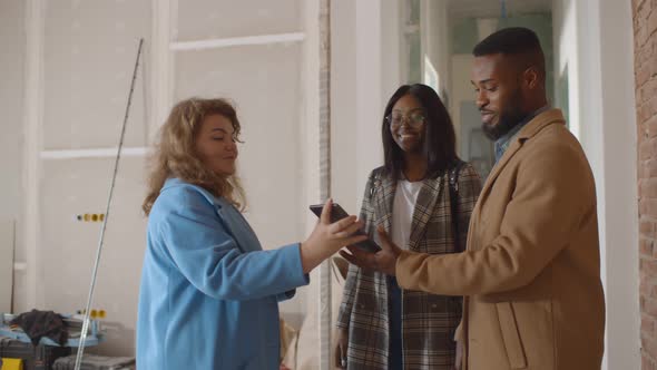 Female Architect Showing House Design Plans on Digital Tablet To Young African Couple alt