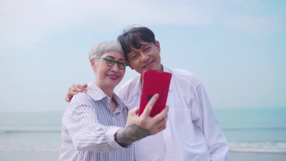A senior woman taking a selfie photo with her partner on the beach. alt